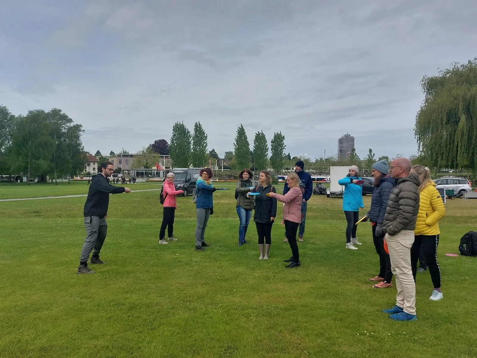 Gruppe von Erwachsenen bei einer Einführung ins Disc Golf auf einer Wiese