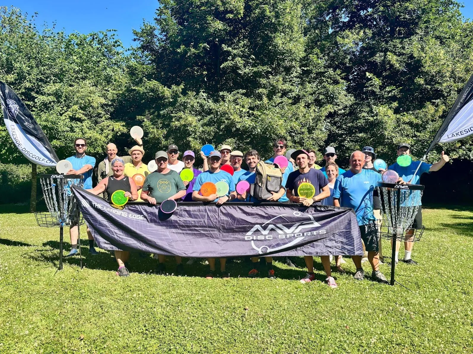 Gruppe mit Discs hinter einem Banner zwischen zwei Disc Golf Körben