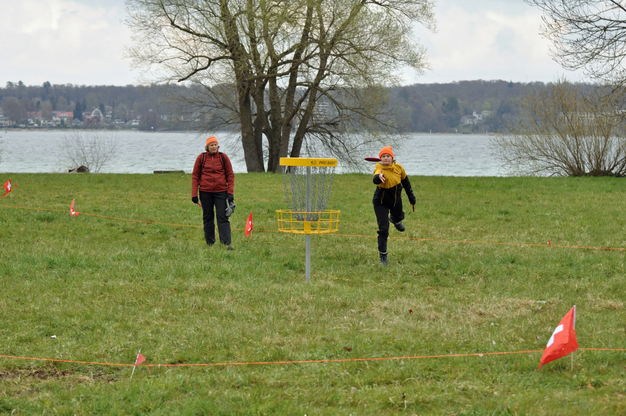 Spielerin beim Putt auf einen gelben Disc Golf Korb, dahinter der Bodensee