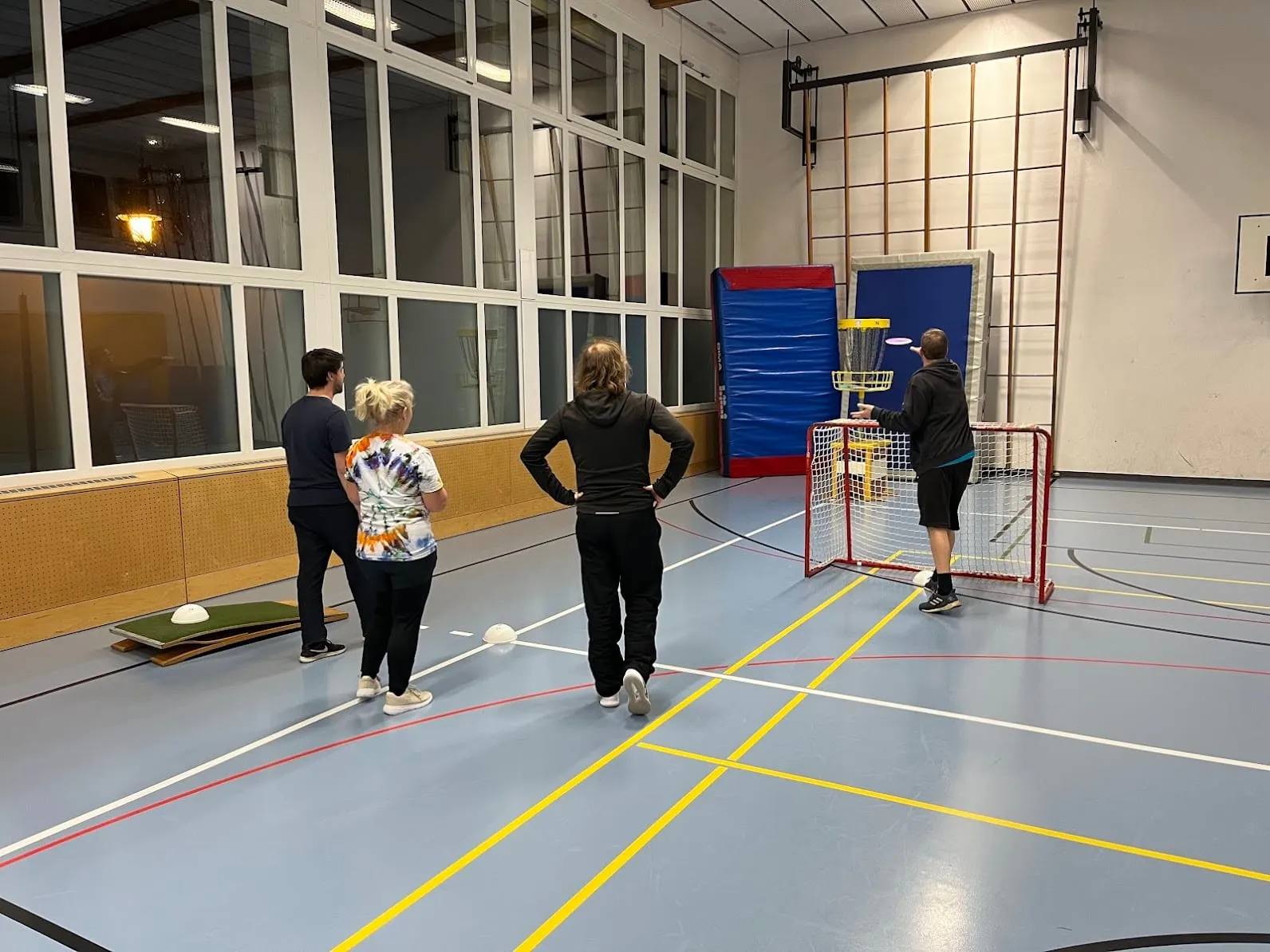 Mehrere Personen in der Sporthalle vor einem Hindernis-Tor mit Disc Golf Korb